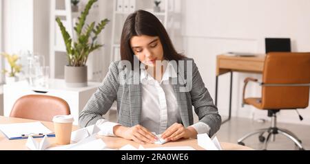Junge Geschäftsfrau, die ein Papierflugzeug am Tisch im Büro macht Stockfoto