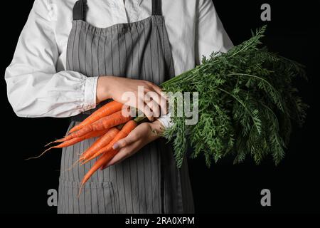 Eine Frau mit einem Haufen frischer Karotten mit Blättern auf schwarzem Hintergrund Stockfoto