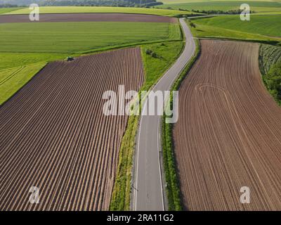 Lange Asphaltstraße zwischen landwirtschaftlichen Flächen mit Erde und Weizen von oben Stockfoto