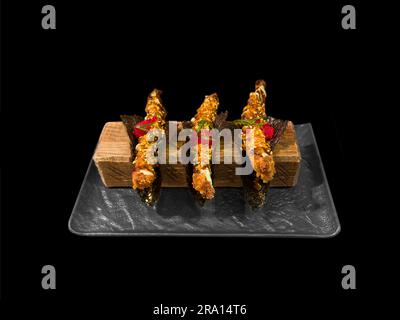 Tempura-Shrimps auf einer schwarzen Platte, isoliert auf schwarzem Hintergrund. Frittierte Shrimps Tempura. Stockfoto