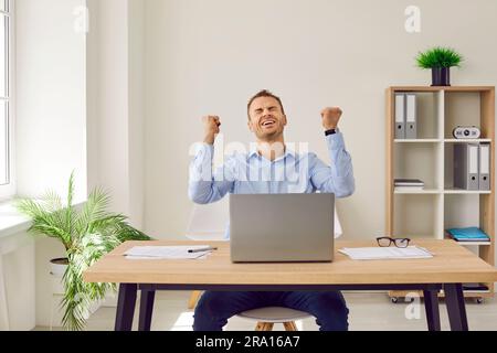 Ein Geschäftsmann, der im Büro sitzt und mit den Händen in den Fäusten Ja-Gesten macht, wie ein Gewinner. Stockfoto