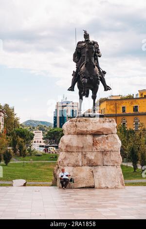 Ein Mann sitzt vor dem Skanderbeg Monument – einem Nationalhereo, der die Osmanen bekämpfte – auf dem Skanderbeg Square, Tirana, Albanien Stockfoto