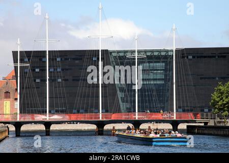 Kopenhagen, Dänemark. 28. Juni 2023. Ein Touristenboot nähert sich der Cirkelbroen (Circle Bridge), entworfen vom dänisch-isländischen Künstler Olafur Eliasson, dessen Masten an ein Segelschiff erinnern. Im Hintergrund ist die Struktur des Den Sorte Diamant (der schwarze Diamant) zu sehen. In den kommenden Tagen findet in Kopenhagen der 28. Weltkongress der Architekten statt. (Zu dpa 'gesundes Bauen' - wie nachhaltig kann Architektur sein?') Kredit: Steffen Trumpf/dpa/Alamy Live News Stockfoto