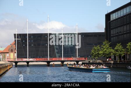 Kopenhagen, Dänemark. 28. Juni 2023. Ein Touristenboot nähert sich der Cirkelbroen (Circle Bridge), entworfen vom dänisch-isländischen Künstler Olafur Eliasson, dessen Masten an ein Segelschiff erinnern. Im Hintergrund ist die Struktur des Den Sorte Diamant (der schwarze Diamant) zu sehen. In den kommenden Tagen findet in Kopenhagen der 28. Weltkongress der Architekten statt. (Zu dpa 'gesundes Bauen' - wie nachhaltig kann Architektur sein?') Kredit: Steffen Trumpf/dpa/Alamy Live News Stockfoto