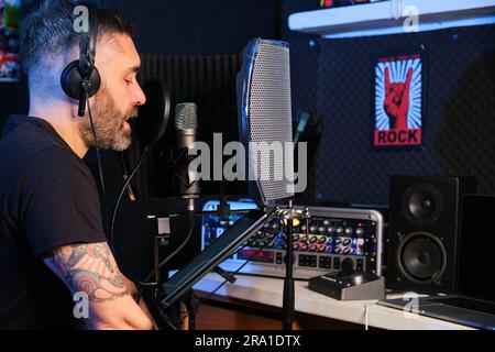 Sprecher in Kopfhörern liest eine Geschichte ins Mikrofon, um sie aufzunehmen. Sprechsprecher im Stimmaufnahmestudio. Stockfoto