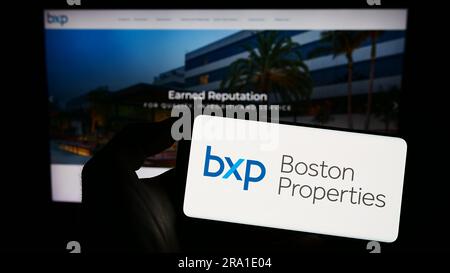 Person, die ein Mobiltelefon mit dem Logo des US-amerikanischen Unternehmens Boston Properties Inc. Besitzt (BXP) auf dem Bildschirm vor der Unternehmenswebseite. Konzentrieren Sie sich auf das Display des Telefons. Stockfoto