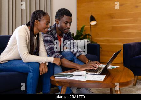 Glückliches afroamerikanisches Paar, das zu Hause Papierkram mit einem Laptop erledigt Stockfoto