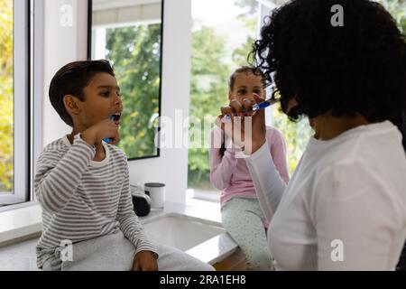 Glückliche, birassische Mutter, Sohn und Tochter, die morgens im Badezimmer Zähne putzen Stockfoto