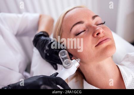 Kaukasische Frau bekommen Gesichtspeeling Verfahren in einer Schönheitsklinik, Nahaufnahme. Verjüngende Gesichtsgasbehandlung. Hydro Air Haut Reinigung Operat Stockfoto