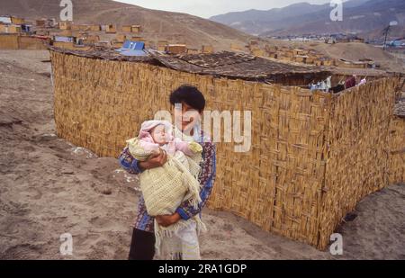 Peru - Mutter mit ihrem Baby vor ihrer aus Schilf gefertigten Hütte in einem Slum nahe Lima in den Dünen des Meeres. Stockfoto