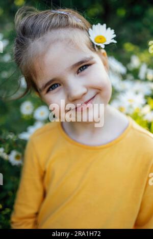 Nahaufnahme des Kinderporträts eines süßen kleinen Mädchens im gelben Hemd bei Kamillenimedow. Der hübsche Junge lächelt beim Aufräumen mit Gänseblümchen auf B Stockfoto