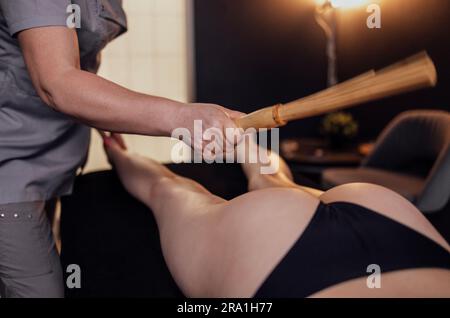 Masseuse macht eine Anti-Cellulite-Massage mit Bambusstäbchen im Spa-Salon. Beinmassage mit Bambusbesen im Schönheitssalon oder in der Klinik. Das Konzept von Stockfoto