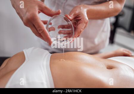 Gesichtslose Masseurin, die während einer entspannenden Massage im Wellnesscenter Öl in die Hand gießt. Körperpflege, Gesundheitskonzept Stockfoto
