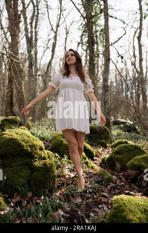 Schneeglöckchen galanthus-Frau. Sie steht in einem weißen Kleid auf einer Wiese mit Schneeglöckchen in einem Frühlingswald Stockfoto