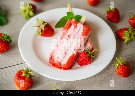 Gekochtes hausgemachtes Erdbeereis auf einem Stock auf einem Teller mit Erdbeeren Stockfoto