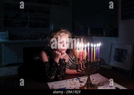 Zwei Schwestern stehen zusammen und sehen Chanukkah Menorah voll beleuchtet an Stockfoto