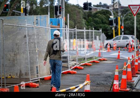 Ein Mann, der auf dem Bürgersteig läuft, mit orangefarbenen Verkehrskegeln auf der einen Seite und Betonblöcken auf der anderen Seite. Straßenarbeiten in Auckland. Stockfoto