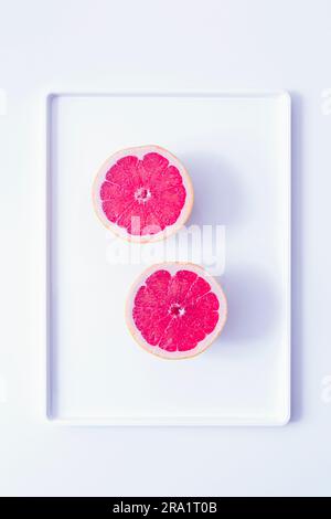 Zwei Hälften einer frischen Grapefruit auf einem Tablett gegen Weiß Stockfoto