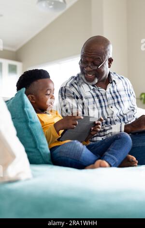 Glücklicher afroamerikanischer Großvater und Enkel, der auf dem Sofa sitzt und ein Tablet benutzt Stockfoto