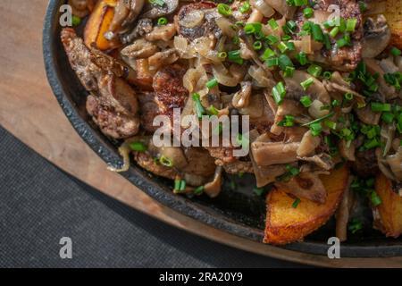 Zarte Hühnerlebern und knusprige Kartoffeln, gekocht in einer gusseisernen Pfanne mit aromatischem Knoblauch, Kräutern und gebratenen Zwiebeln. Ein köstliches und tröstliches Mea Stockfoto