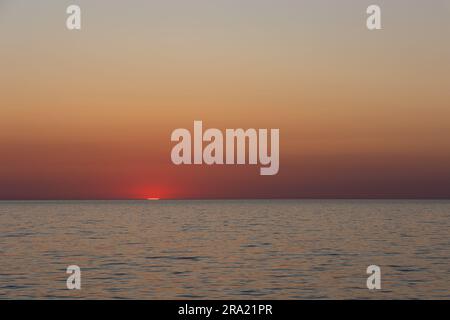 Die letzten Sonnenstrahlen gehen über einem ruhigen Meer unter. Statische Aufnahme während eines wolkenlosen Abends Stockfoto