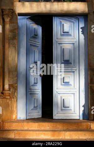 Teilweise geöffnete blaue Eingangstür mit Ornamenten in warmem Nachmittagslicht, Catas Altas, Minas Gerais, Brasilien Stockfoto