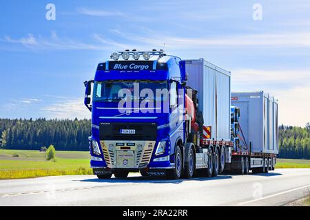 Der blaue Volvo FH16 Lkw mit Palfingerkran von Blue Cargo Oy zieht an einem sonnigen Tag zwei tragbare Fahrerhäuser auf einem Anhänger entlang der Autobahn 2. 9. Juni 2023. Stockfoto