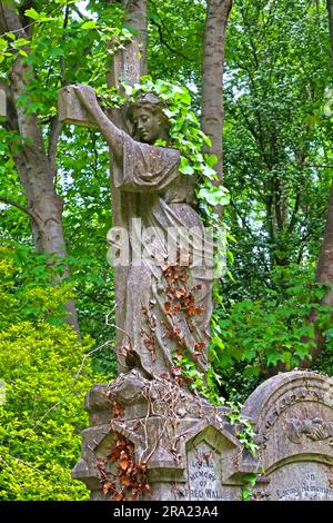 Efeu bedeckte Grabsteine Engel und Kreuz umgeben von dichter Vegetation auf dem Highgate Cemetery, einem historischen viktorianischen Grabplatz in Nord-London, England Stockfoto