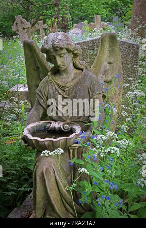 Steinengelgrabmarkierung umgeben von Wildblumen und bewachsener Vegetation auf dem Highgate Cemetery, einem historischen viktorianischen Grabplatz im Norden Londons Stockfoto