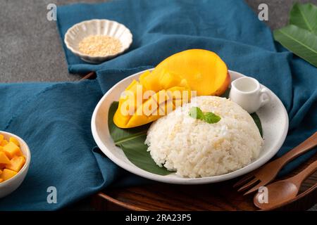 Köstlicher klebriger Reis aus thailändischer Mango mit geschnittenen frischen Mangofrüchten auf einem Teller mit grauem Tischhintergrund. Stockfoto