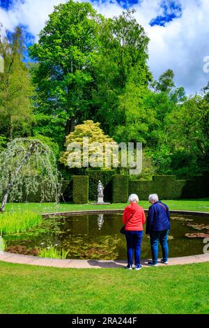 Zwei Besucher genießen die friedliche Ruhe des ruhigen Wassers im kreisförmigen Pool Garden am Knightshayes Court, nr Tiverton, Devon, England, Großbritannien Stockfoto