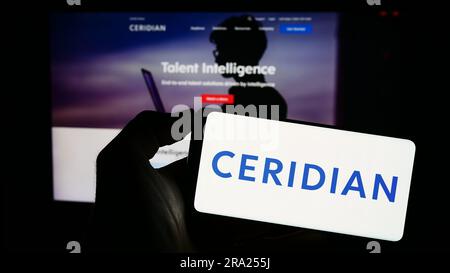 Person, die ein Mobiltelefon mit dem Logo des US-amerikanischen Softwareunternehmens Ceridian HCM Holding Inc. Auf dem Bildschirm vor der Webseite hält. Konzentrieren Sie sich auf das Display des Telefons. Stockfoto