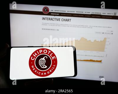 Person, die ein Mobiltelefon mit dem Logo der amerikanischen Firma Chipotle Mexican Grill Inc. Auf dem Bildschirm vor der Webseite hält. Konzentrieren Sie sich auf das Display des Telefons. Stockfoto