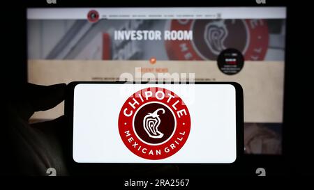 Person, die ein Mobiltelefon mit dem Logo der US-amerikanischen Firma Chipotle Mexican Grill Inc. Auf dem Bildschirm vor der Business-Webseite hält. Konzentrieren Sie sich auf das Display des Telefons. Stockfoto