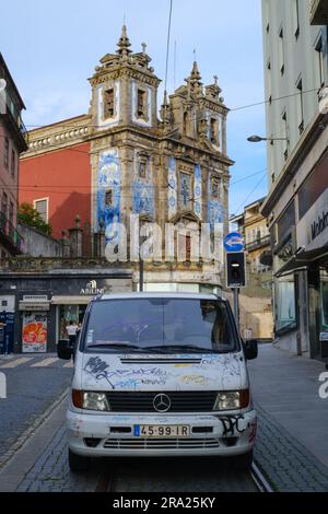 Ein mit Graffiti überdachter Van vor der gefliesten Kirche Igreja de Santo Ildefonso in Porto, Portugal, 2023. Stockfoto