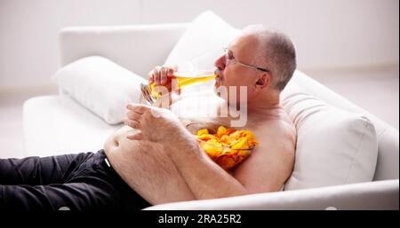 Übermäßiges Essen mit Junk Food, Bier trinken und Fernsehen Stockfoto
