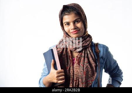 Ein hübsches, junges, indisches, muslimisches Mädchen mit Büchern in der Hand, mit lächelndem Gesicht auf weißem Hintergrund Stockfoto