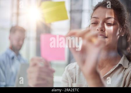 Ihre Vision zum Leben erwecken. Aufnahme einer selbstbewussten Geschäftsfrau, die ihrem Kollegen mit Haftnotizen an einer Glaswand im Büro eine Idee vorstellt. Stockfoto