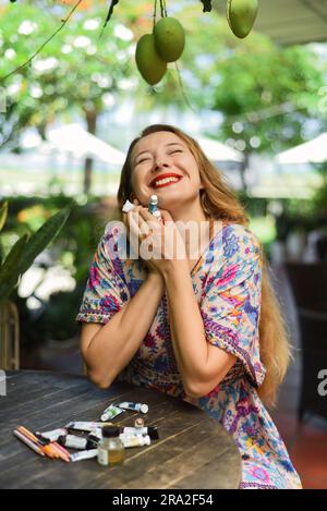 Porträt einer wunderschönen blonden Künstlerin und Illustratorin, die am Tisch sitzt und ihre Acrylfarben in der Hand hält Stockfoto