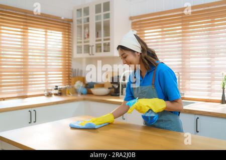 Die geschickte asiatische Hausfrau verwendet mühelos eine Tischdecke und ein Sprühgerät in ihrer Küche und demonstriert so ihre Expertise bei der Schaffung eines sauberen und einladenden s Stockfoto