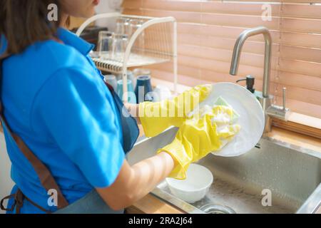 Nahaufnahme einer asiatischen Hausfrau, die in der Küche des Hauses Geschirr spült und Gummihandschuhe trägt Stockfoto