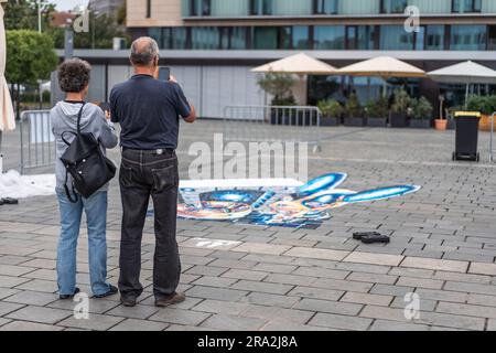 Kaiserslautern, Deutschland. 30. Juni 2023. Fußgänger, die mit ihrem Smartphone Bilder von 3D Bildern machen. Elf internationale Künstler aus 6 Ländern verwandelten den Stiftsplatz (Platz) in dreidimensionale Kunst, wobei das Thema „Digitalisierung und intelligente Stadt“ dieses Jahr stand. 3D Street Art nutzt die Perspektive, um eine optische Illusion des Weltraums zu erzeugen. Die Besucher konnten alle Künstler bei der Arbeit drei Tage lang beobachten. Dies ist der dritte und letzte Tag der Veranstaltung. Kredit: Gustav Zygmund/Alamy News Stockfoto