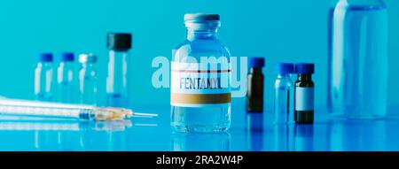 Eine simulierte Durchstechflasche Fentanyl neben einer Spritze und einige andere Durchstechflaschen auf einem blauen Tisch, in einem Panoramaformat zur Verwendung als Webbanner Stockfoto