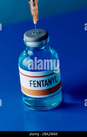 Nahaufnahme einer simulierten Fentanyl-Durchstechflasche mit einer Spritze, die in ihren Stopfen auf einem blauen Tisch gesteckt wurde Stockfoto