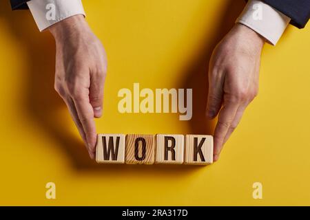 Das Wort ARBEIT ist in Holzwürfeln in schwarzen Buchstaben auf gelbem Hintergrund geschrieben. Stockfoto