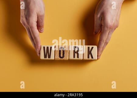 Das Wort ARBEIT ist in Holzwürfeln in schwarzen Buchstaben auf gelbem Hintergrund geschrieben. Stockfoto