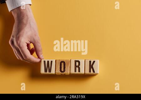 Das Wort ARBEIT ist in Holzwürfeln in schwarzen Buchstaben auf gelbem Hintergrund geschrieben. Stockfoto