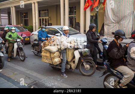 Ein vietnamesischer Mann sitzt auf einem Motorrad-Roller, überladen mit Säcken Zement und Ziegeln im Verkehr auf Trang Tien, im Zentrum von Hanoi Vietnam. Stockfoto