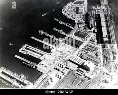 Luftaufnahme des US Naval Dry Dock. Dieses Foto ist eine Luftaufnahme des US Naval Dry Dock mit BB-61 USS Iowa in Dry Dock #3, USS Bunker Hill in East Jetty und AP-21 USS Wakefield am Pier. 1943-01-01T00:00:00. Nordostregion (Boston, MA). Fotodruck. Abteilung der Marine. Erster Marinebezirk. Büro des stellvertretenden Stabschefs für Verwaltung. Büro des Historischen Offiziers. Ca. 1941-ca. 1946. Die Verwaltungsgeschichte des ersten Marinestreifens im Zweiten Weltkrieg Stockfoto