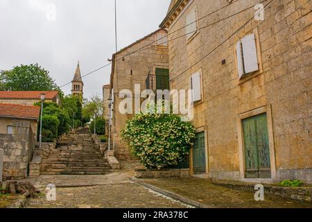 Eine historische Wohnstraße in der Stadt Nerezisca auf der Insel Brac in Kroatien. Die Kirche unserer Lieben Frau vom Berg Carmel ist im Hintergrund Stockfoto